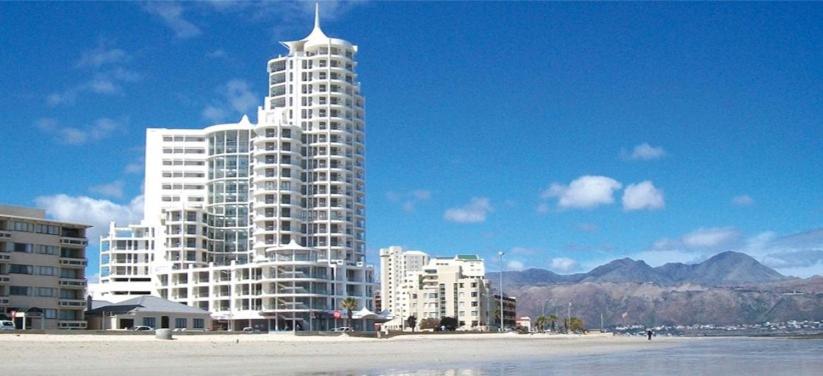 a tall white building on the beach next to the ocean at 302 Hibernian Towers Self Catering Accommodation in Strand