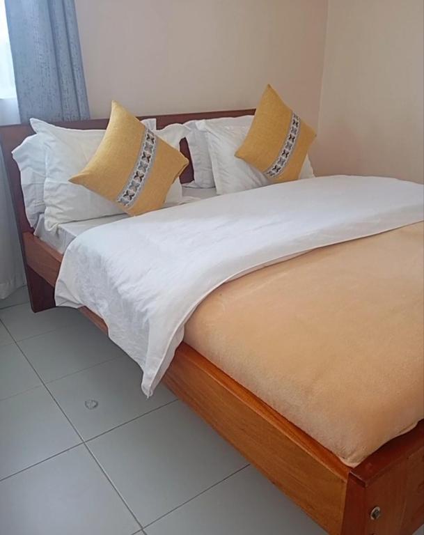 a bed with white sheets and yellow pillows at The Elite havens in Nairobi