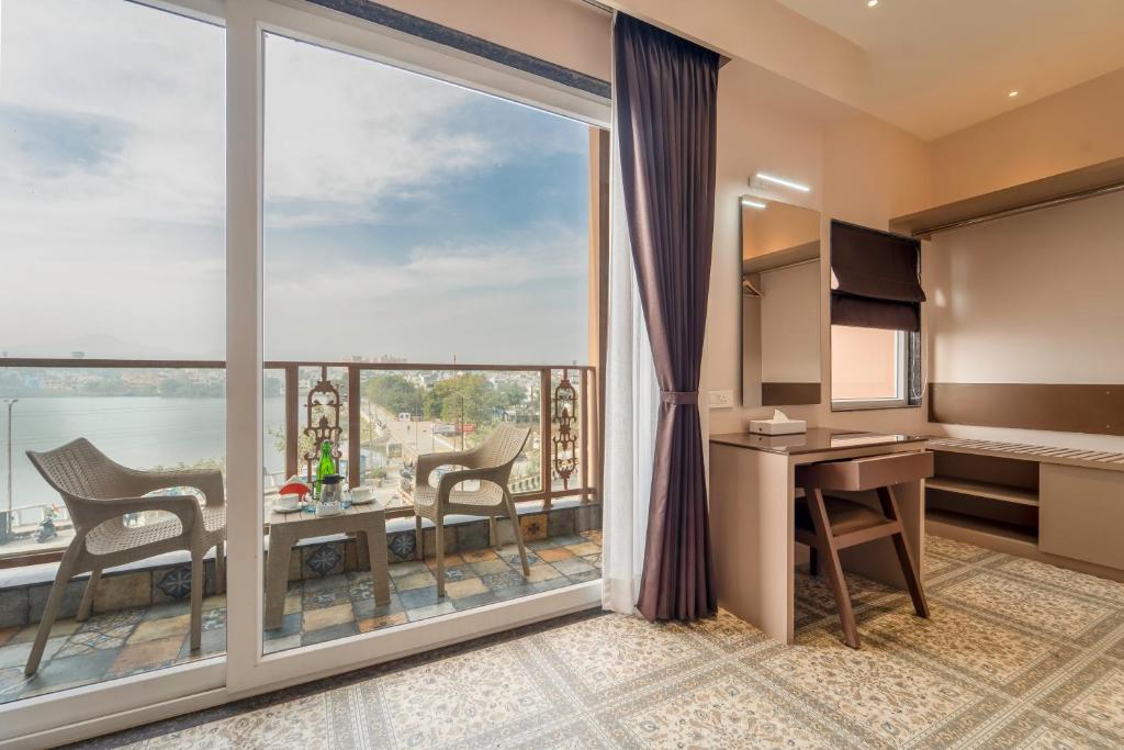 a hotel room with a large window and a desk and chairs at Lakeside Leisure A Lake View Hotel in Udaipur