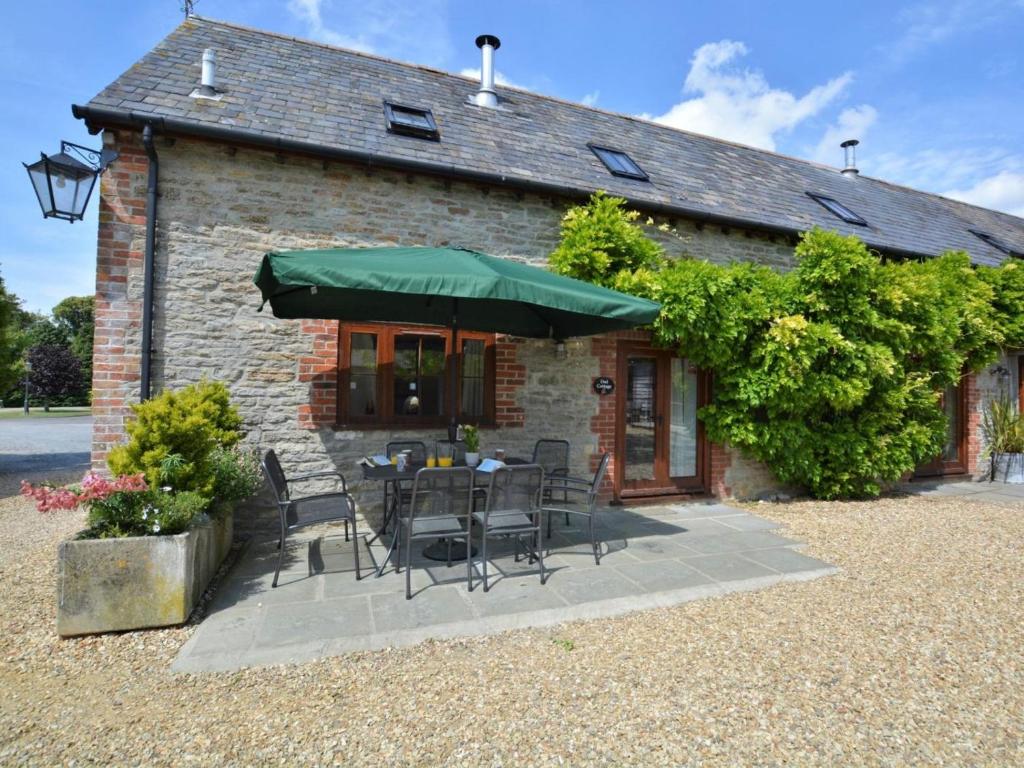 a patio with chairs and a table with a green umbrella at 4 Bed in Sherborne oc-folow in Long Burton