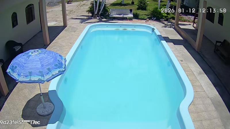 a blue swimming pool with an umbrella next to a house at Chácara braga in Itanhaém