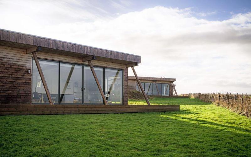 a building in a field of grass with a fence at Jog Lodge 7 By Together Travel - 3 Bed in John O Groats