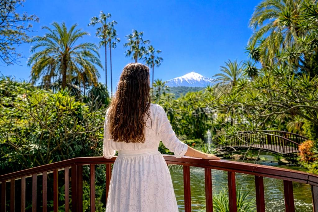a woman standing on a balcony looking at a mountain at Hotel Botanico y Oriental Spa Garden in Puerto de la Cruz