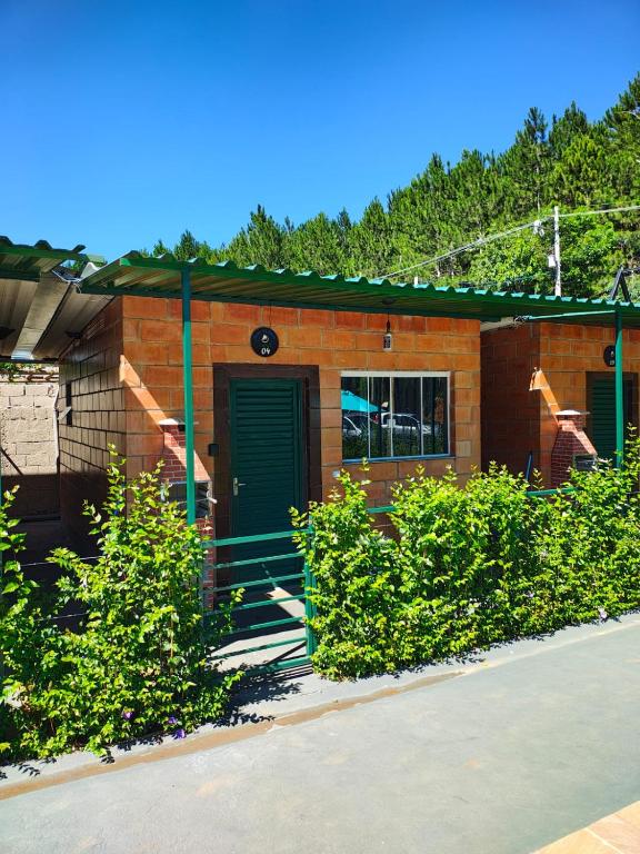a brick house with a green door and bushes at Chalé do Mamute in Atibaia