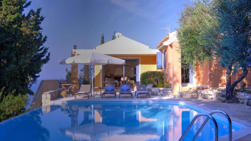 a swimming pool with chairs and an umbrella next to a house at Villa Pelagos in Arvanitakaíïka