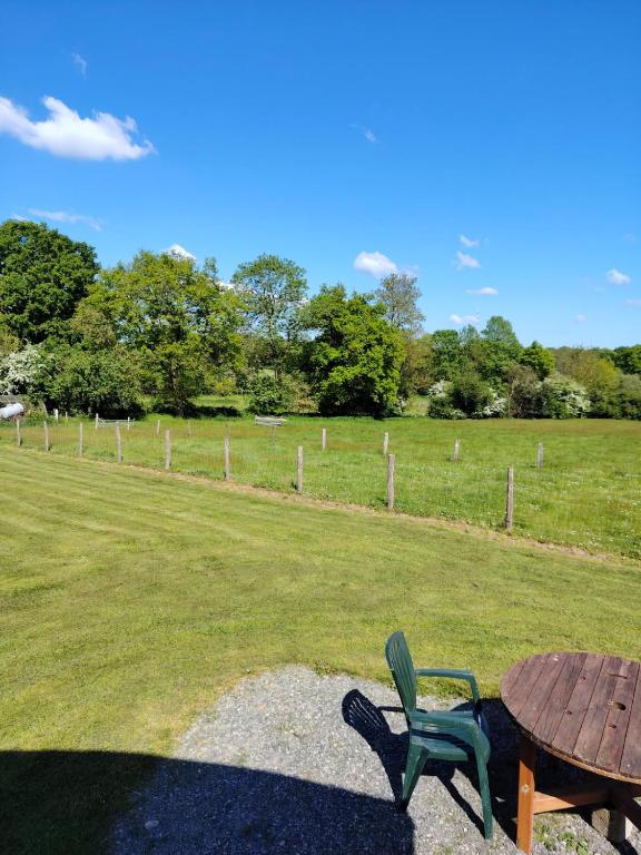 a wooden table and a green chair next to a field at La roulotte de Rochavelle in Chiché