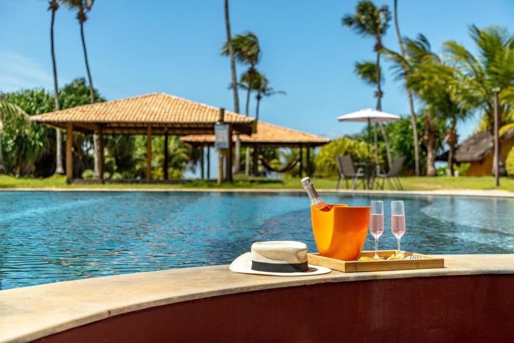 a swimming pool with a table with glasses and a knife and a hat at Refúgio Gostoso in São Miguel do Gostoso