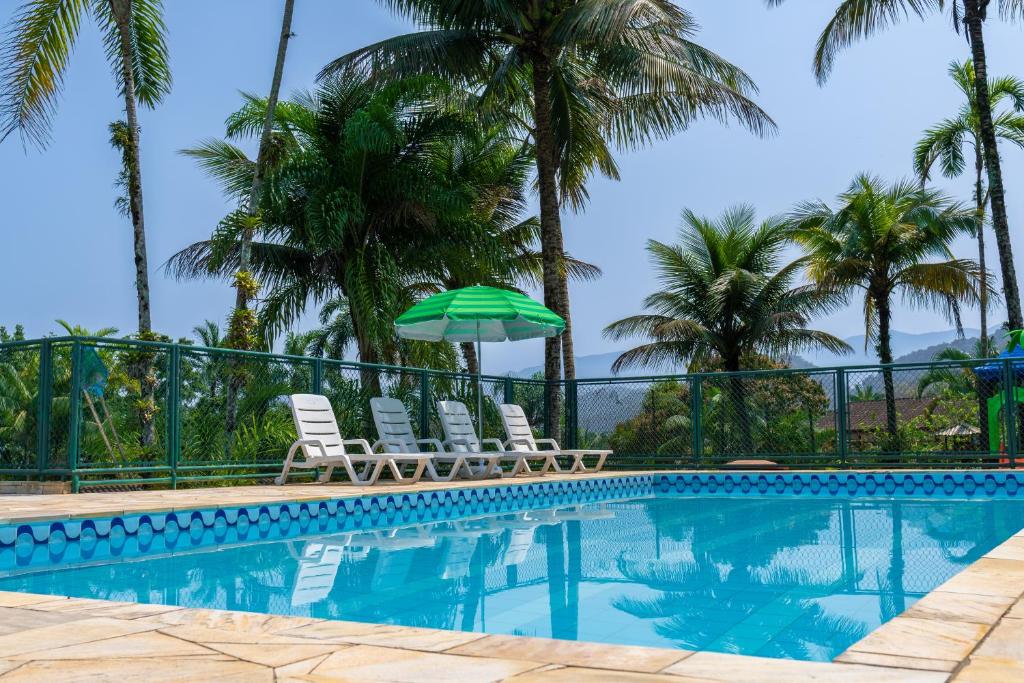 a swimming pool with two chairs and a green umbrella at Marencanto Pousada in Ubatuba