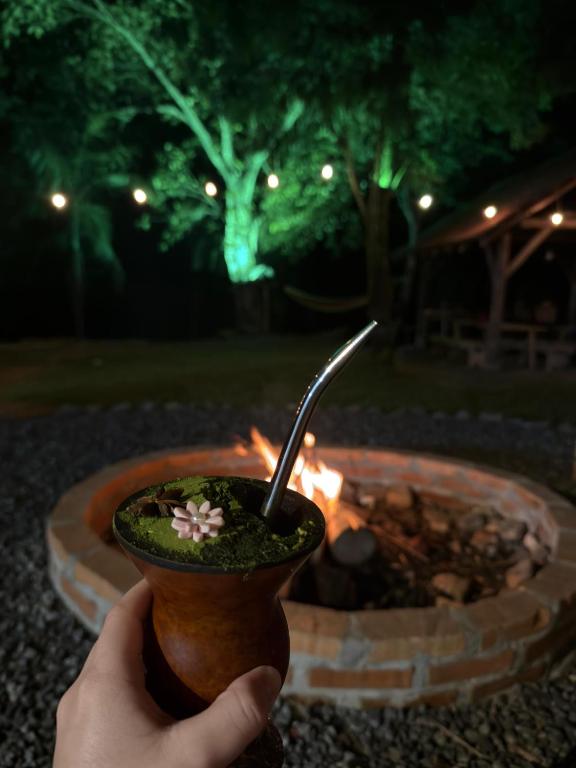 a person holding a drink in a cup next to a fire pit at Rancho300 - Quiriri - Joinville in Joinville
