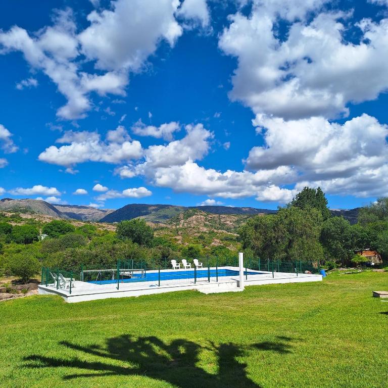 a pool in a field with a blue sky and clouds at Cabañas El Refugio de Juan in Mina Clavero