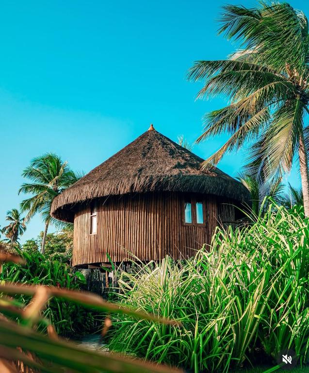 a hut with a thatched roof and palm trees at Carneiros Paradiso in Praia dos Carneiros