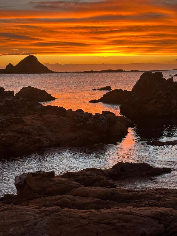 a sunset over the ocean with rocks in the water at Epic Ocean Views & Outdoor bath in Wellington