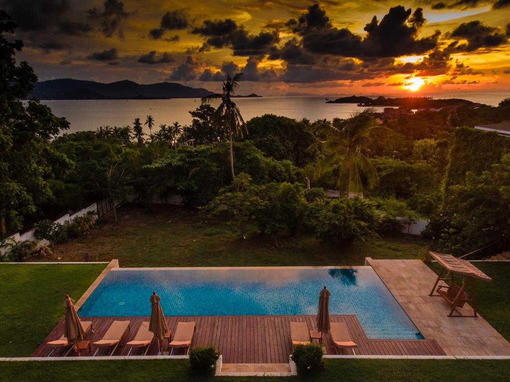 a pool with chairs and a sunset in the background at Baan Apsara - Stunning Sea View 3 Bed Pool Villa in Choeng Mon Beach