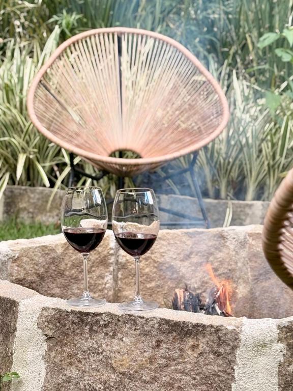two glasses of wine sitting next to a fire pit at Casa 05 Vale Boa Vista - Refúgio Moderno em Condomínio Exclusivo in Teresópolis