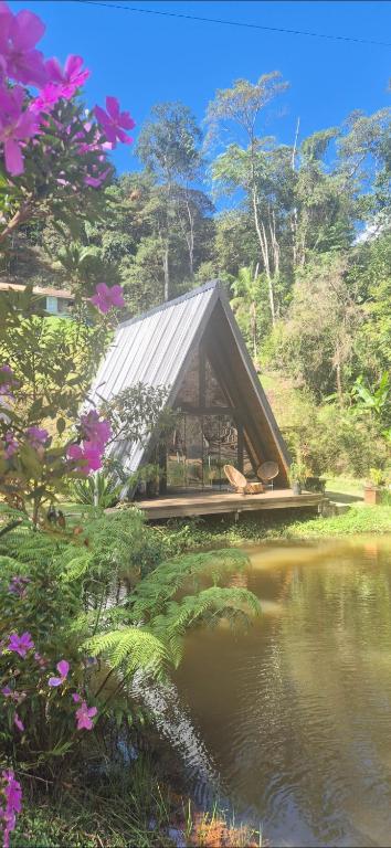 a building with a metal roof next to a pond at Chalé Suíço com Jacuzzi in Marechal Floriano