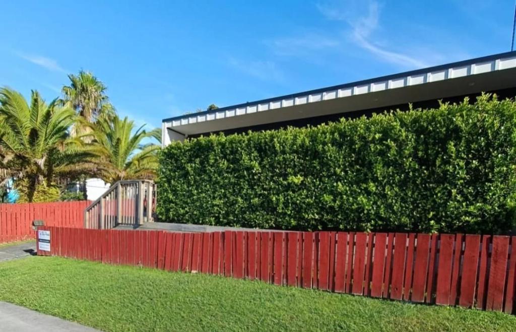 Eine Hecke vor einem Gebäude mit einem roten Zaun in der Unterkunft The Tiny Abode in Snells Beach