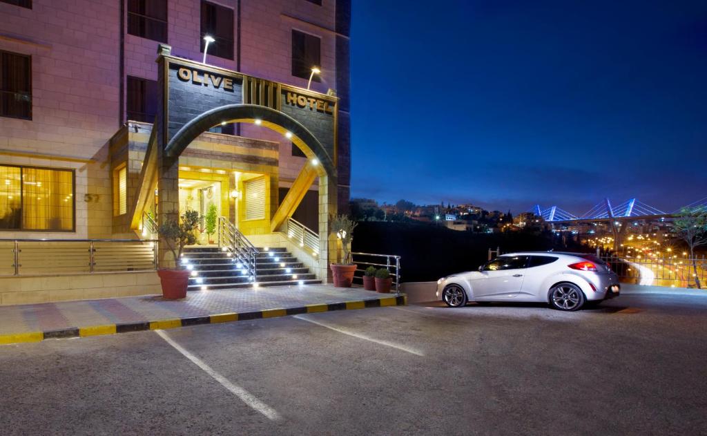 a white car parked in a parking lot in front of a building at Olive Hotel Amman in Amman