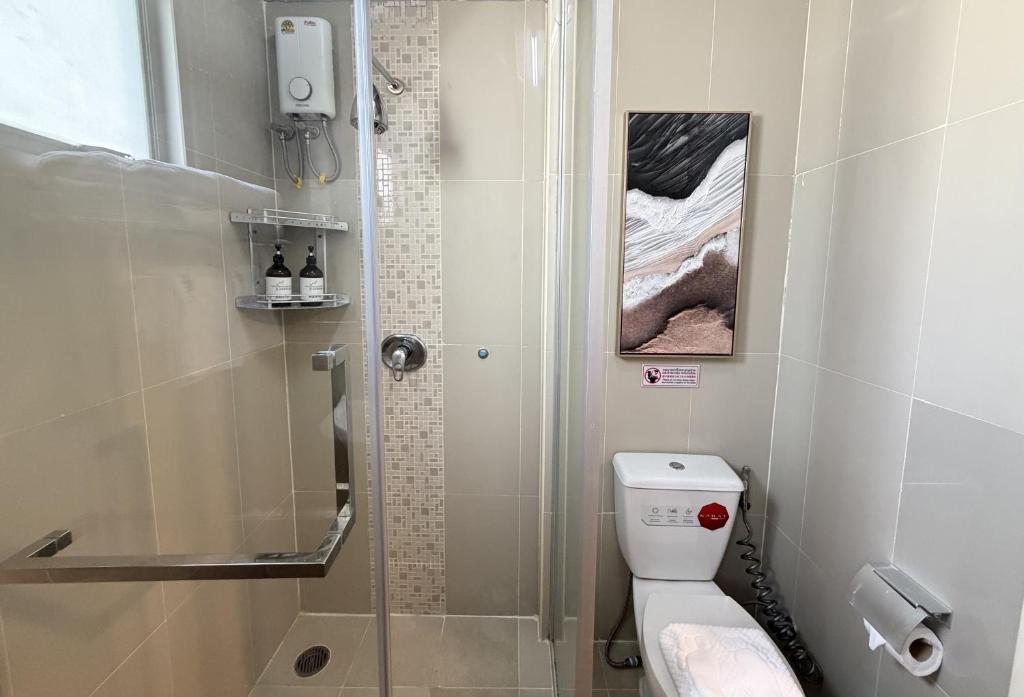 A compact tiled bathroom with a shower, toilet, and narrow glass partition.