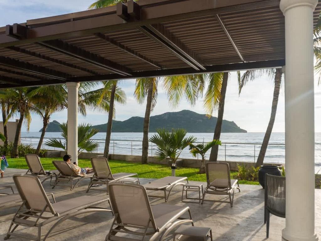 a man sitting on a patio with chairs and the ocean at Luxe Oceanfront Condo in Golden Zone in Mazatlán