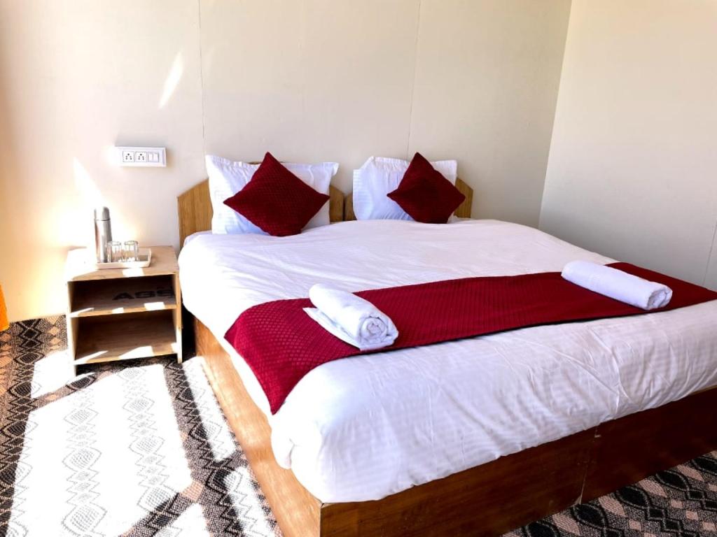 a bedroom with a bed with white sheets and red pillows at zoz camp pangong lake in Lukung