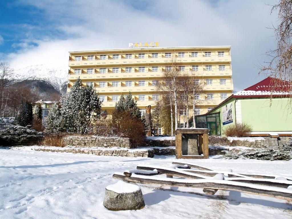 a hotel in the snow with a building in the background at Hotel Palace in Nový Smokovec