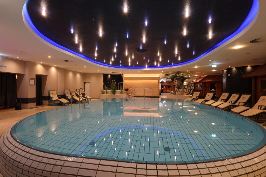a large swimming pool in a large room with chairs at Mauritius Hotel & Therme in Cologne
