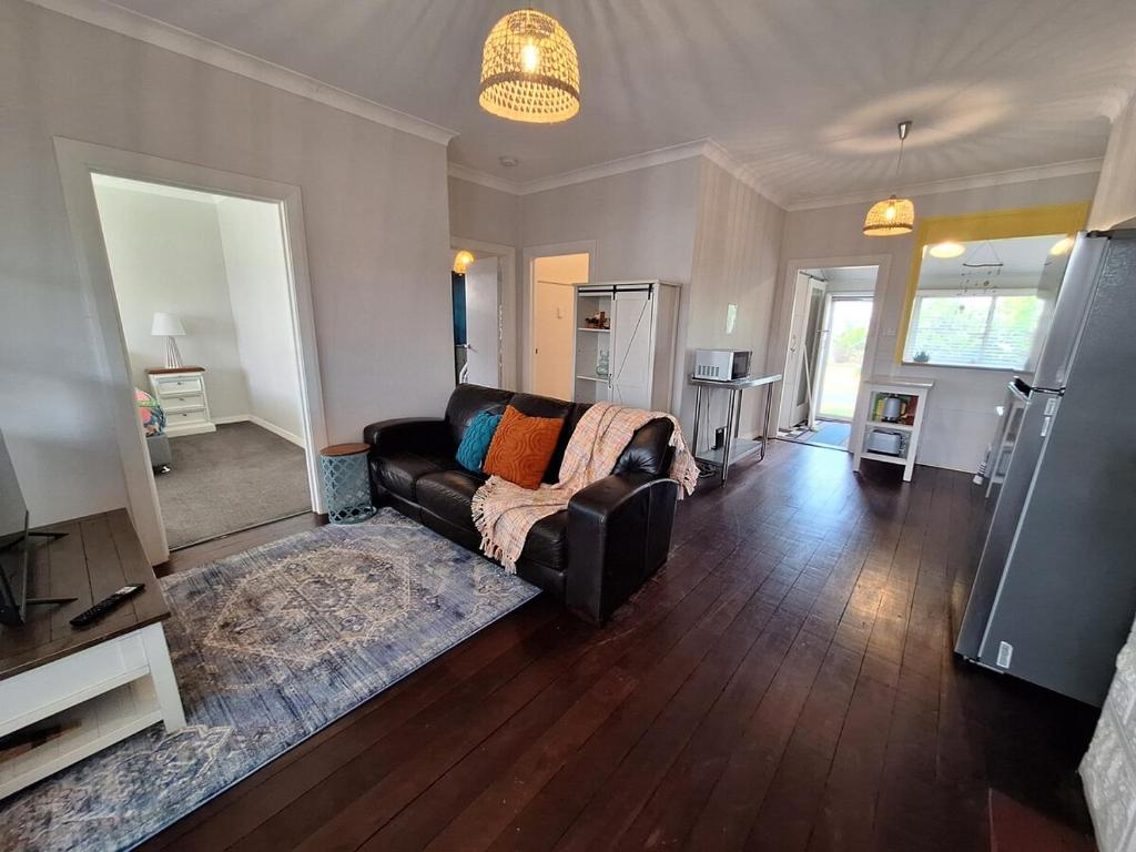 a living room with a leather couch and wooden floors at South Bunbury Beach Shack in Bunbury
