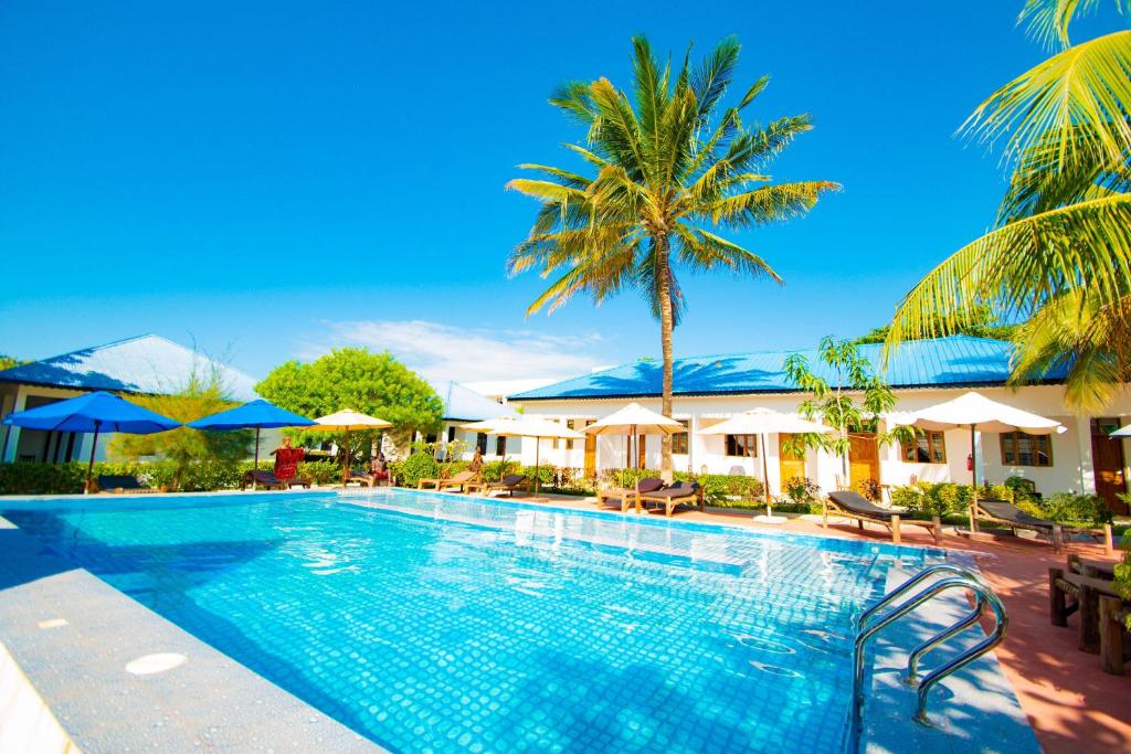 a pool at a resort with palm trees and umbrellas at Kigwedeni Villas in Nungwi