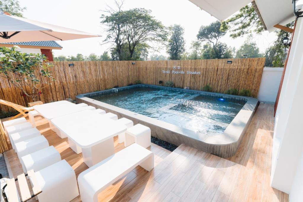 a swimming pool with white furniture and a wooden fence at Tenki poolvilla srisaket in Ban Phia Nam