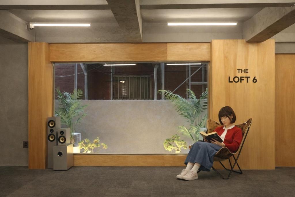 a woman sitting in a chair reading a book at The loft 6 in Busan