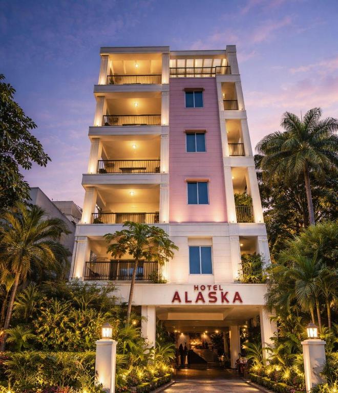 a tall white building with palm trees in front of it at Hotel Alaska in Patna