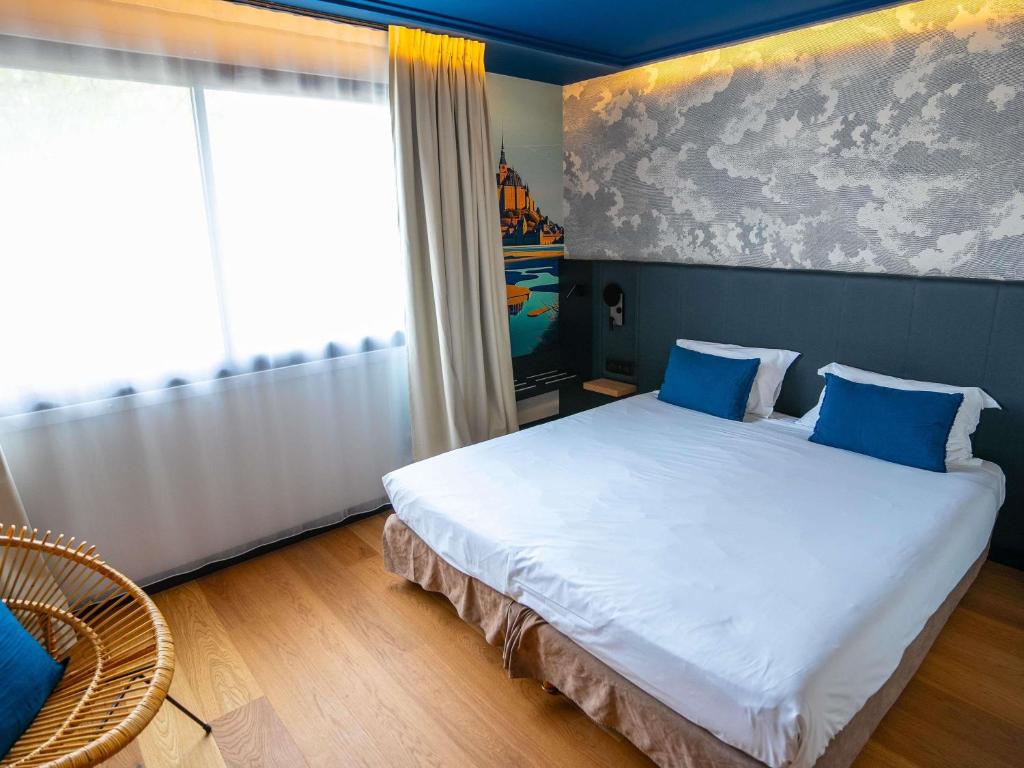 a bedroom with a large white bed with blue pillows at Mercure Mont Saint Michel in Le Mont Saint Michel