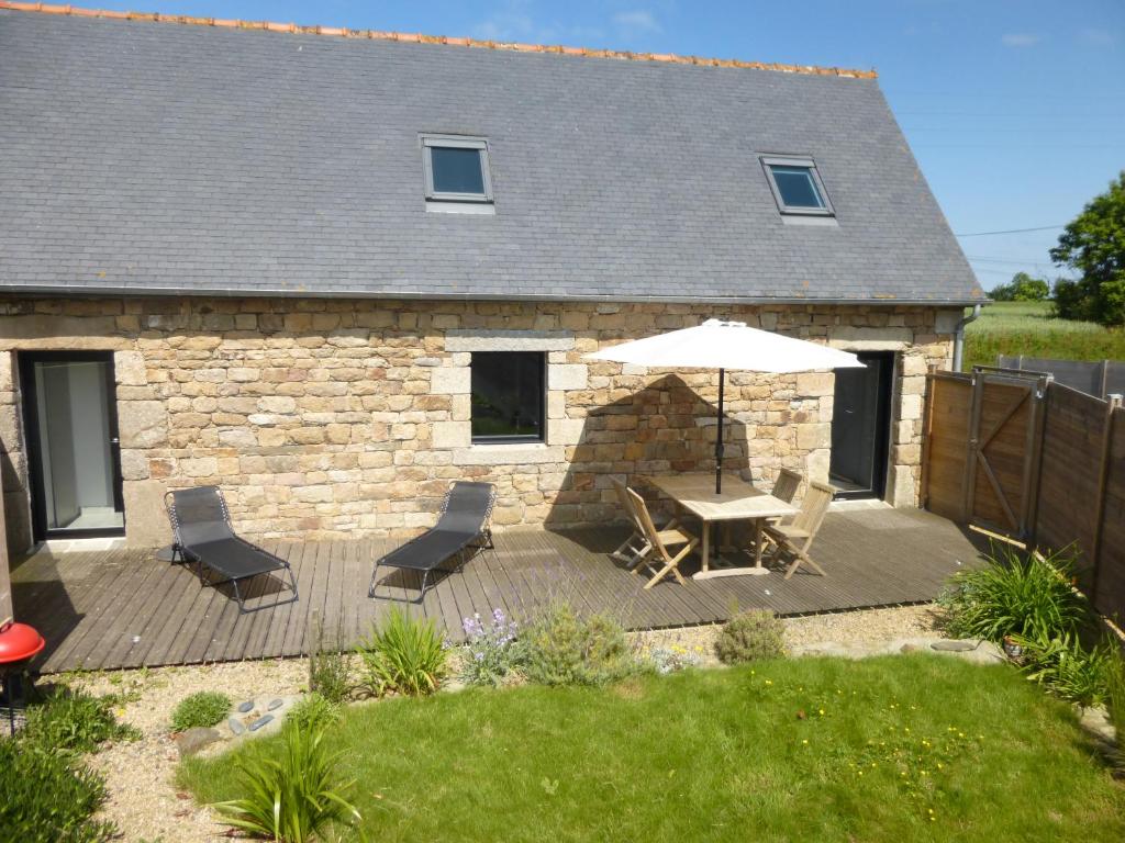 een houten terras met een tafel en stoelen en een parasol bij Gite entre Terre et Mer in Ploumilliau