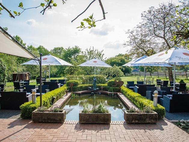a garden with a pond with umbrellas and tables and chairs at Restaurant-Hotel Haus Mühlenbrock in Schermbeck