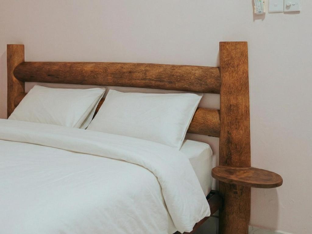 a bed with a wooden head board with white pillows at The Sandscape Fuvahmulah in Fuvahmulah
