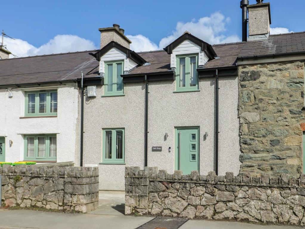 a white house with green windows and a stone wall at Hen Siop in Llanfairpwllgwyngyll