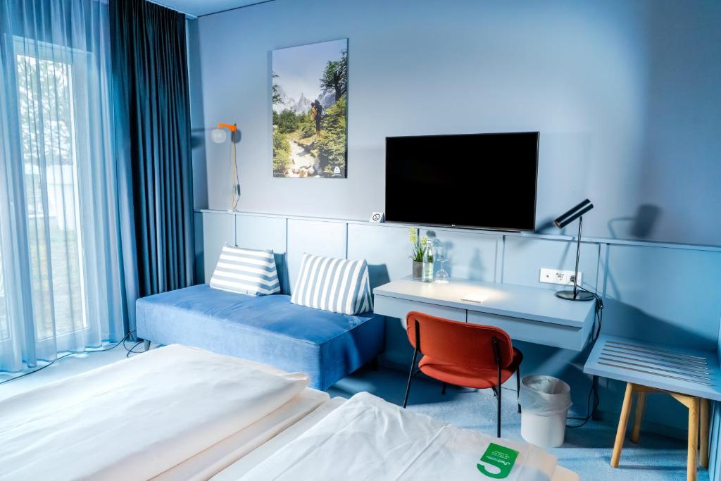 a blue room with a bed and a desk and a tv at Stay2Munich Hotel & Serviced Apartments in Brunnthal
