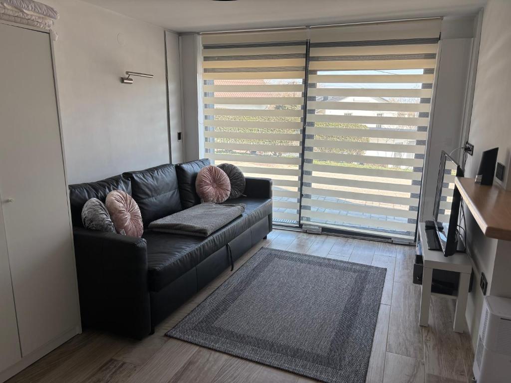 a black leather couch in a living room with a large window at Trinity in Balatonalmádi