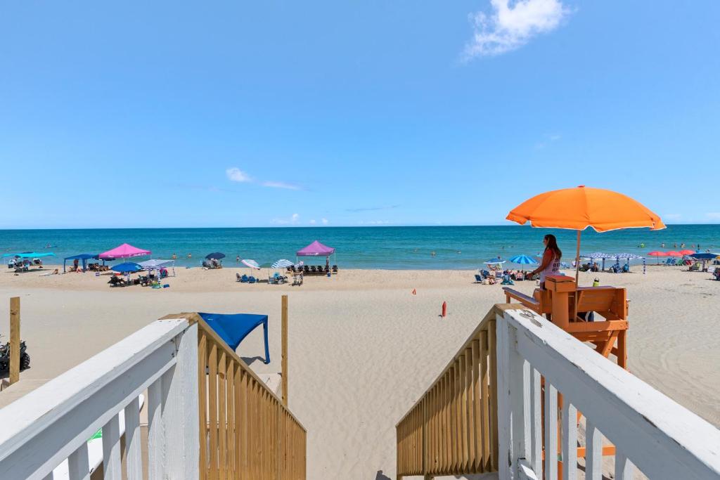 a woman sitting in a chair under an umbrella on the beach at Seaside Sea Esta in Corolla