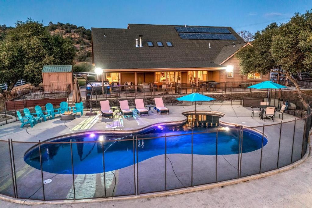 a pool with chairs and umbrellas in front of a house at Mountain Elegance w/ pool, spa, projector in Coarsegold