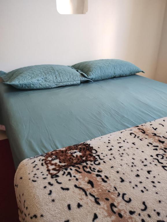 a bed with a blue comforter and two pillows at Pousada Aconchego in São Mateus