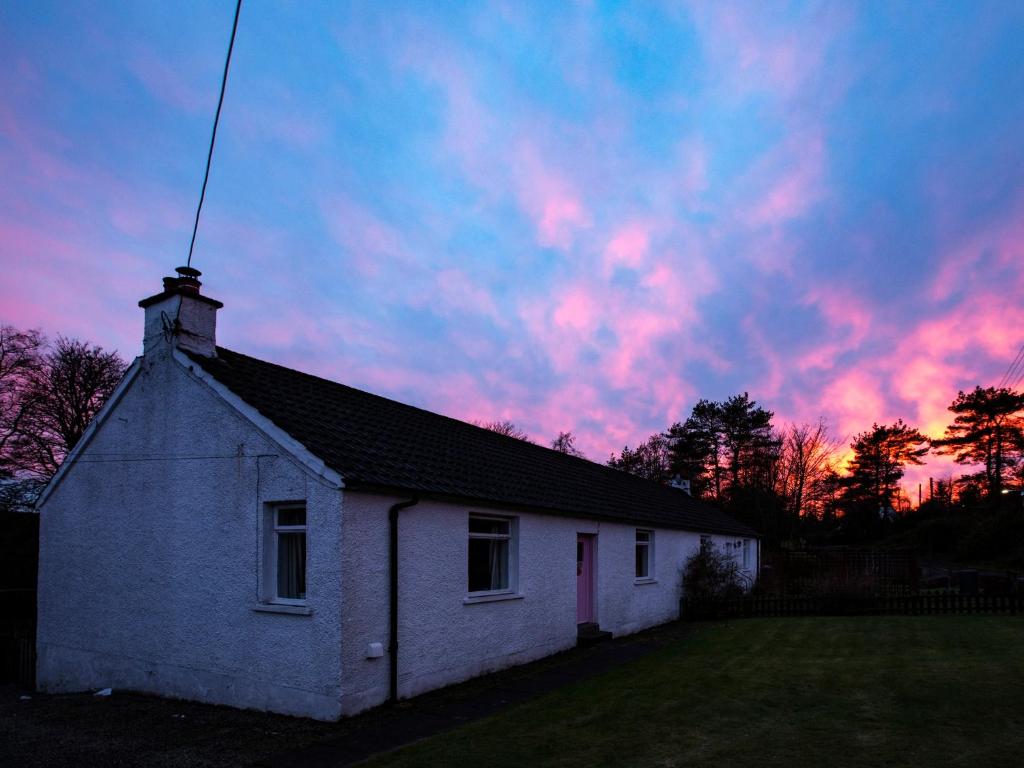 a white house with a sunset in the sky at Culsharg Cottage in Bargrennan