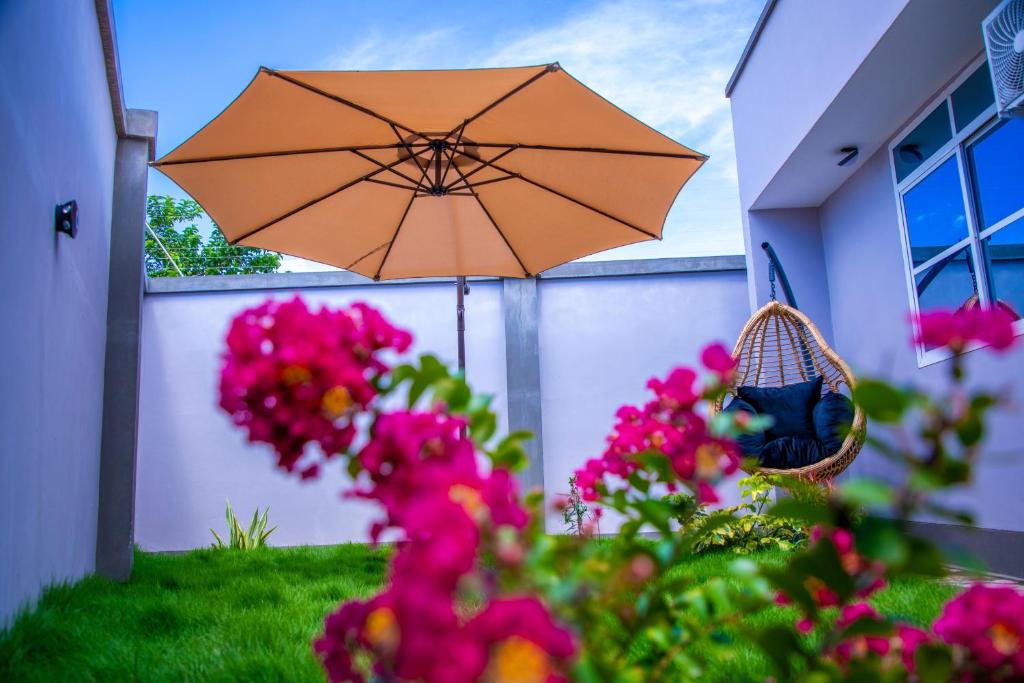 an umbrella in front of a house with pink flowers at Uhondo Apartments in Dodoma
