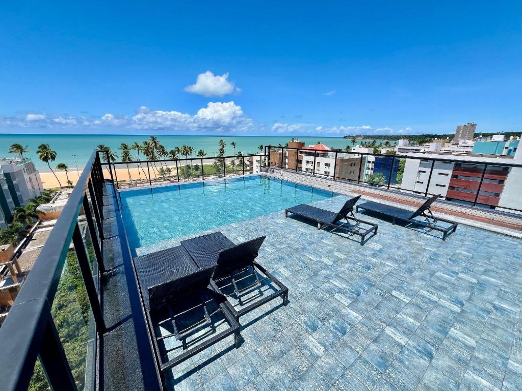 a swimming pool on the roof of a building with chairs at Cabo Branco - Legacy Suítes in João Pessoa