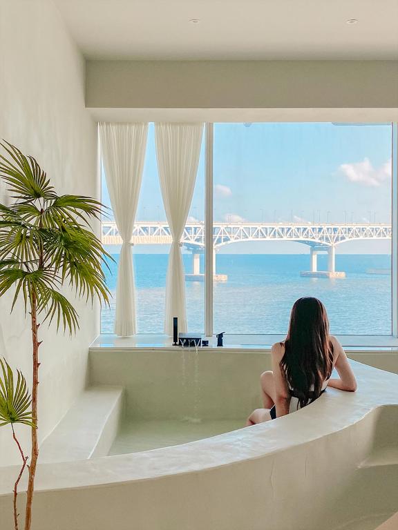 a woman sitting on a bath tub looking out at the ocean at Meomulda Subyeon in Busan