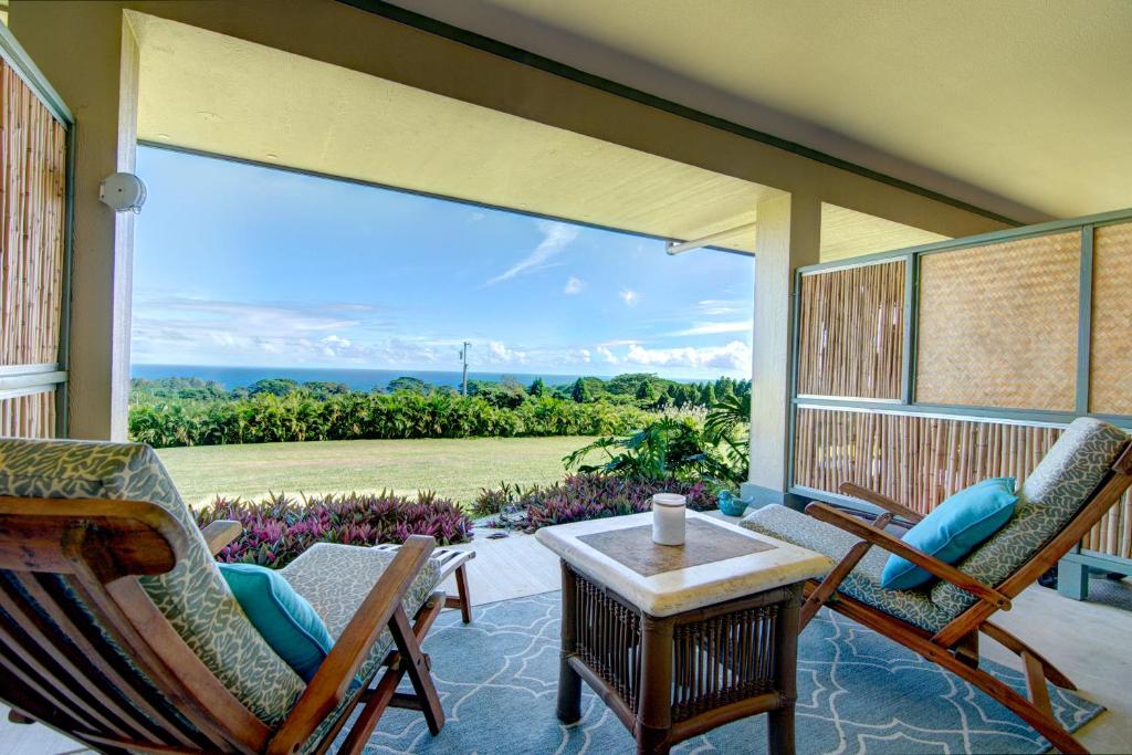 une terrasse couverte avec des chaises, une table et une grande fenêtre dans l'établissement Mahana House Country Inn, à North Hilo