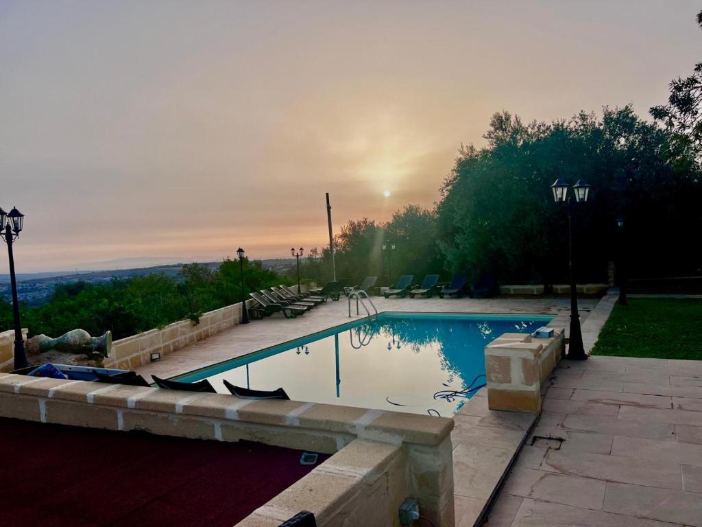 a swimming pool with a sunset in the background at Casale Ciricó tra Catania e Siracusa in Carlentini