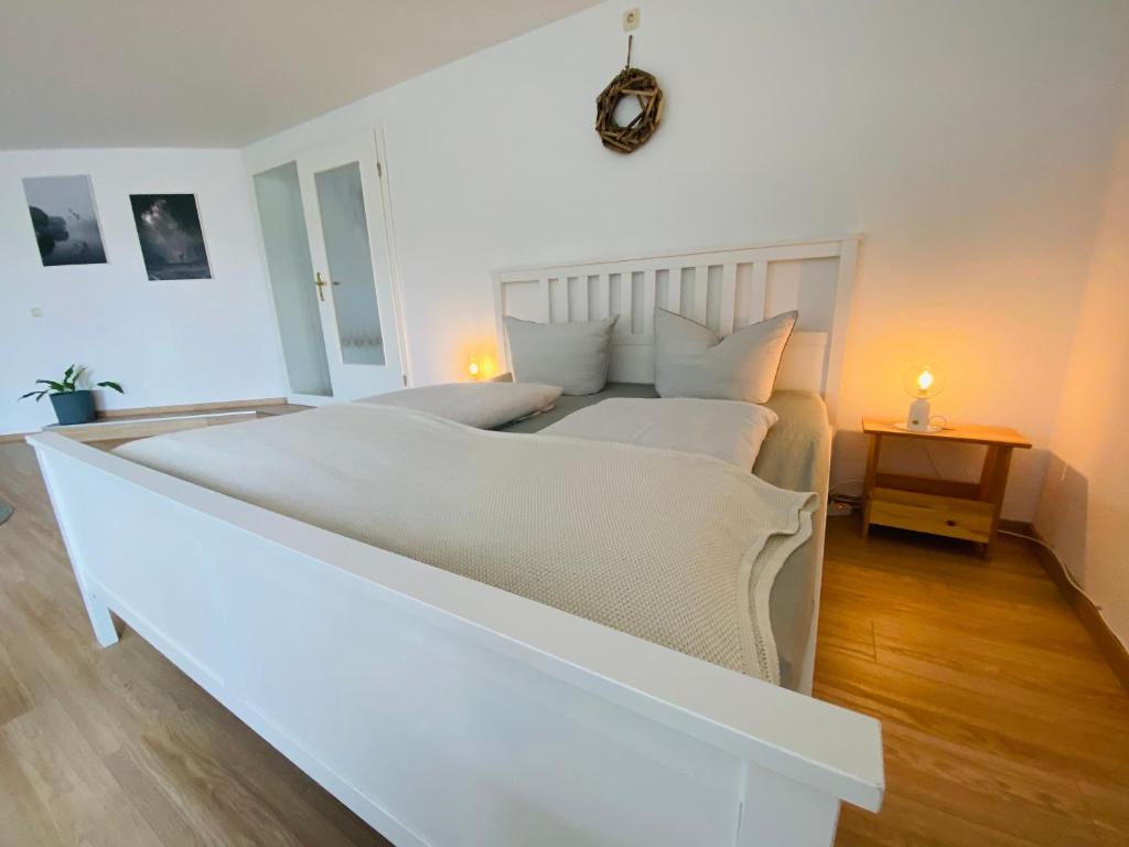 a white bedroom with a large white bed and a table at Ferienwohnung Am Steinberg in Nauendorf