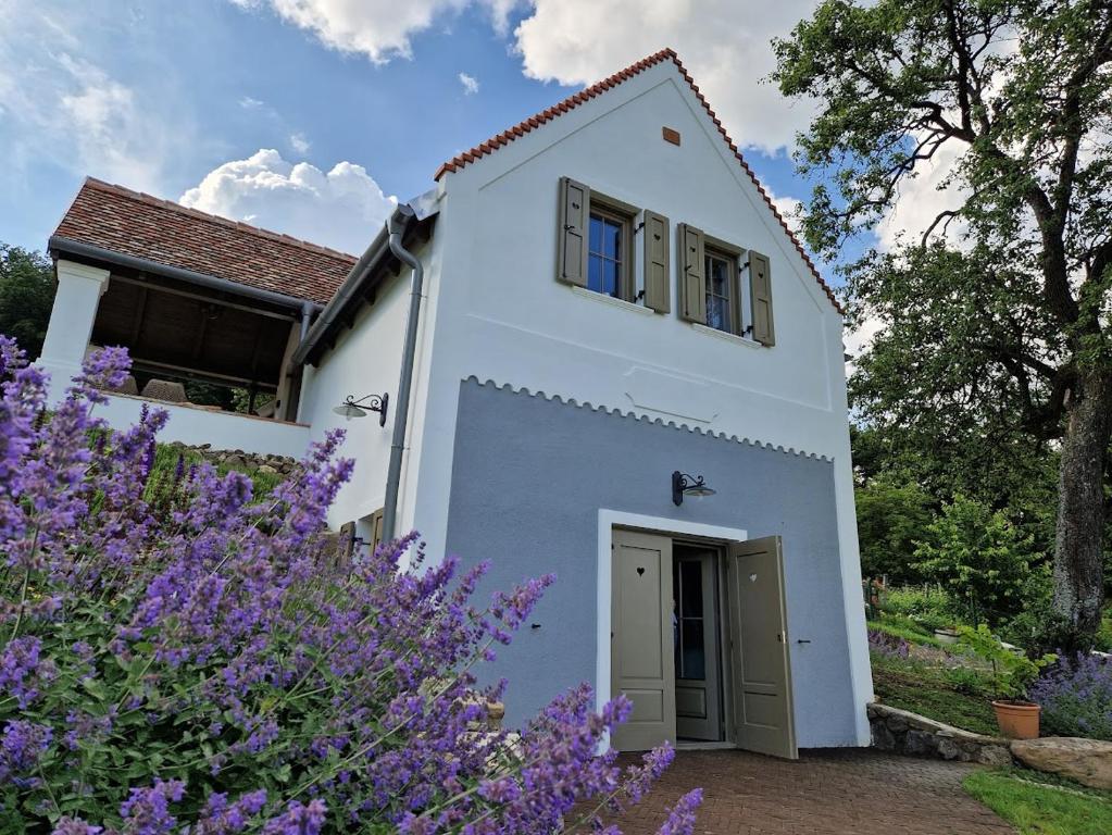 a white house with purple flowers in front of it at Bagolyvölgy Tulkó Ház in Balatonhenye