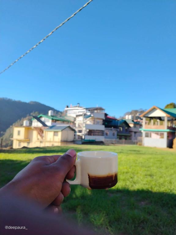 a person holding a cup of coffee in a field at Indu Homestay in Shimla
